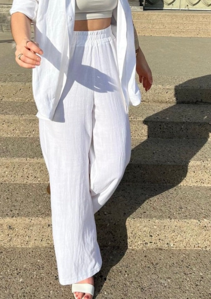 A picture of a woman wearing the classic linen pants in white and paring them with the staple blouse for a complete look.