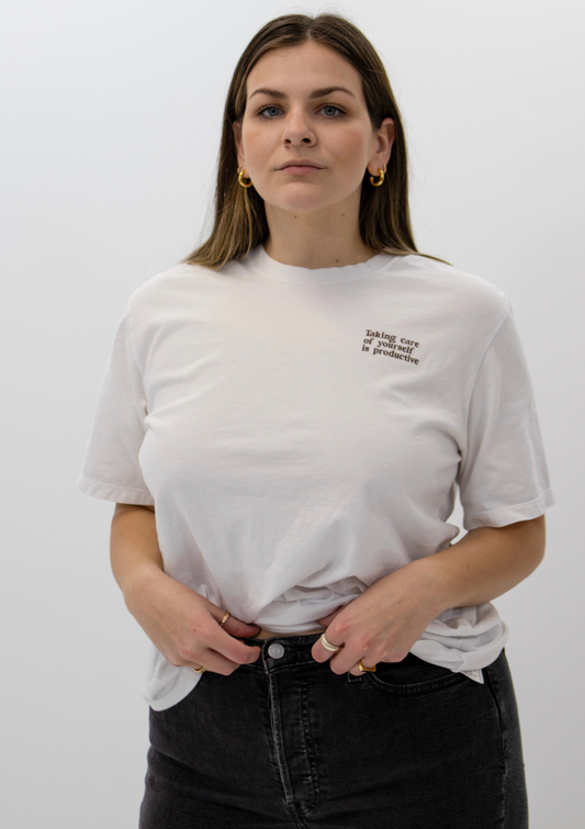 A woman, looking at us, is wearing the "take care tee" made from pre-shrunk cotton
