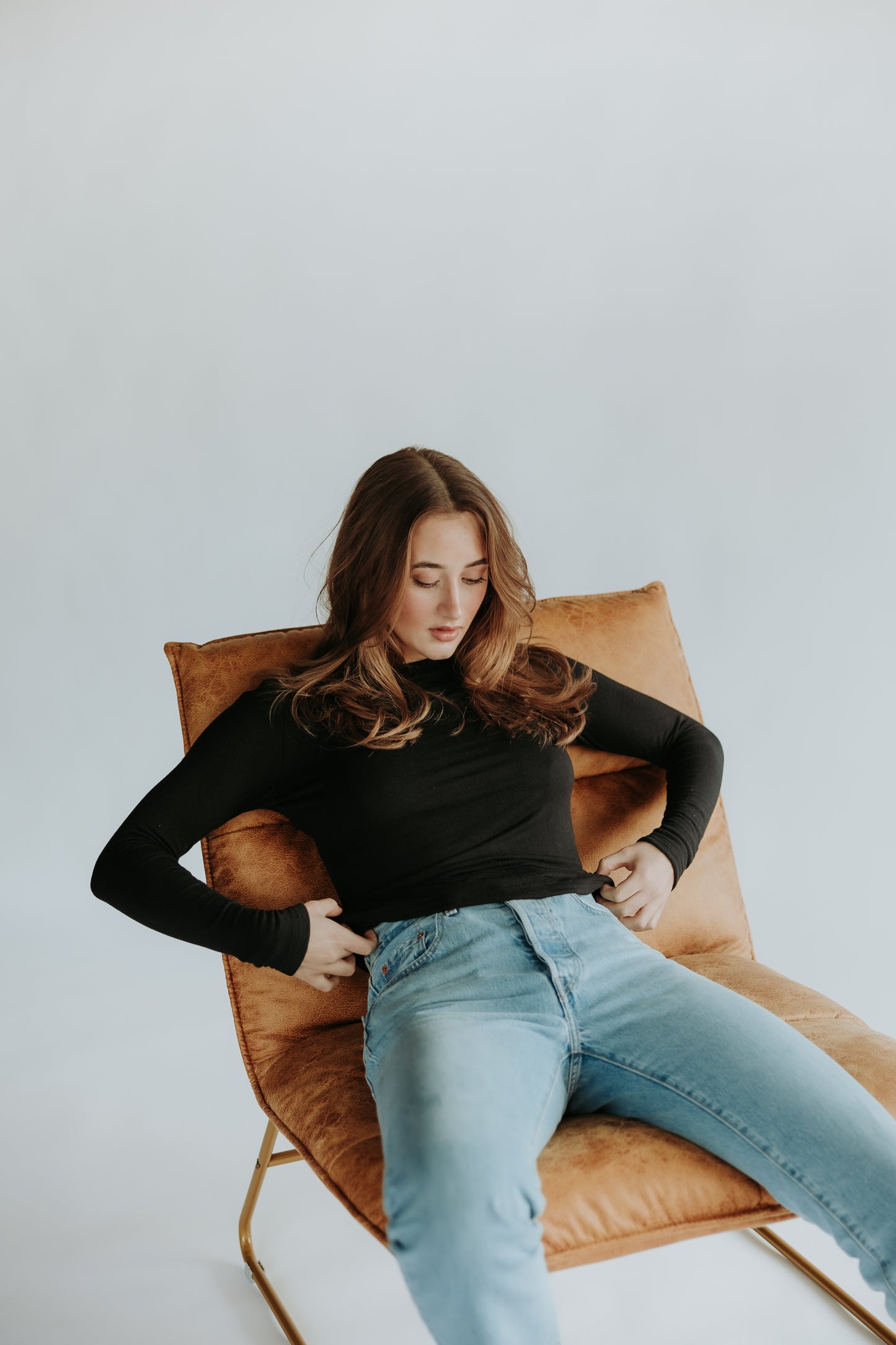 A woman is sitting on a chair, fixing her pants and wearing the double layer buttery long sleeve from SEVE&CO in the color true black