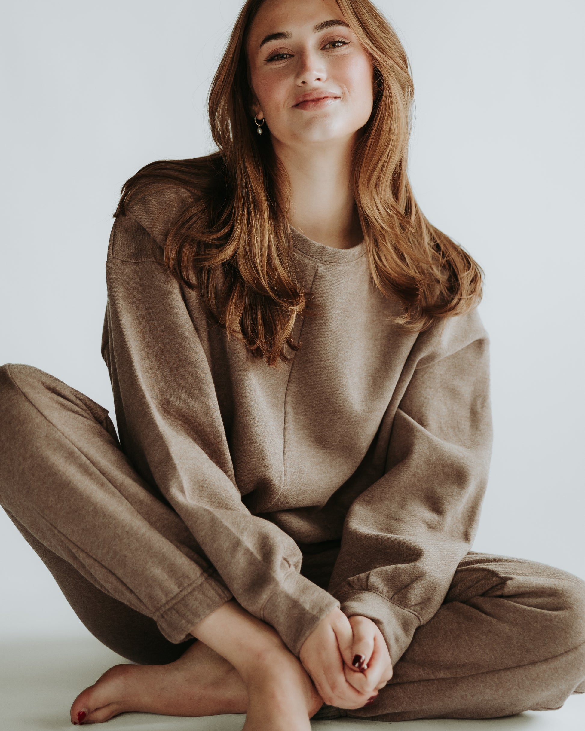 A woman is sitting on the ground and wearing the two-pieces fleece set in brown