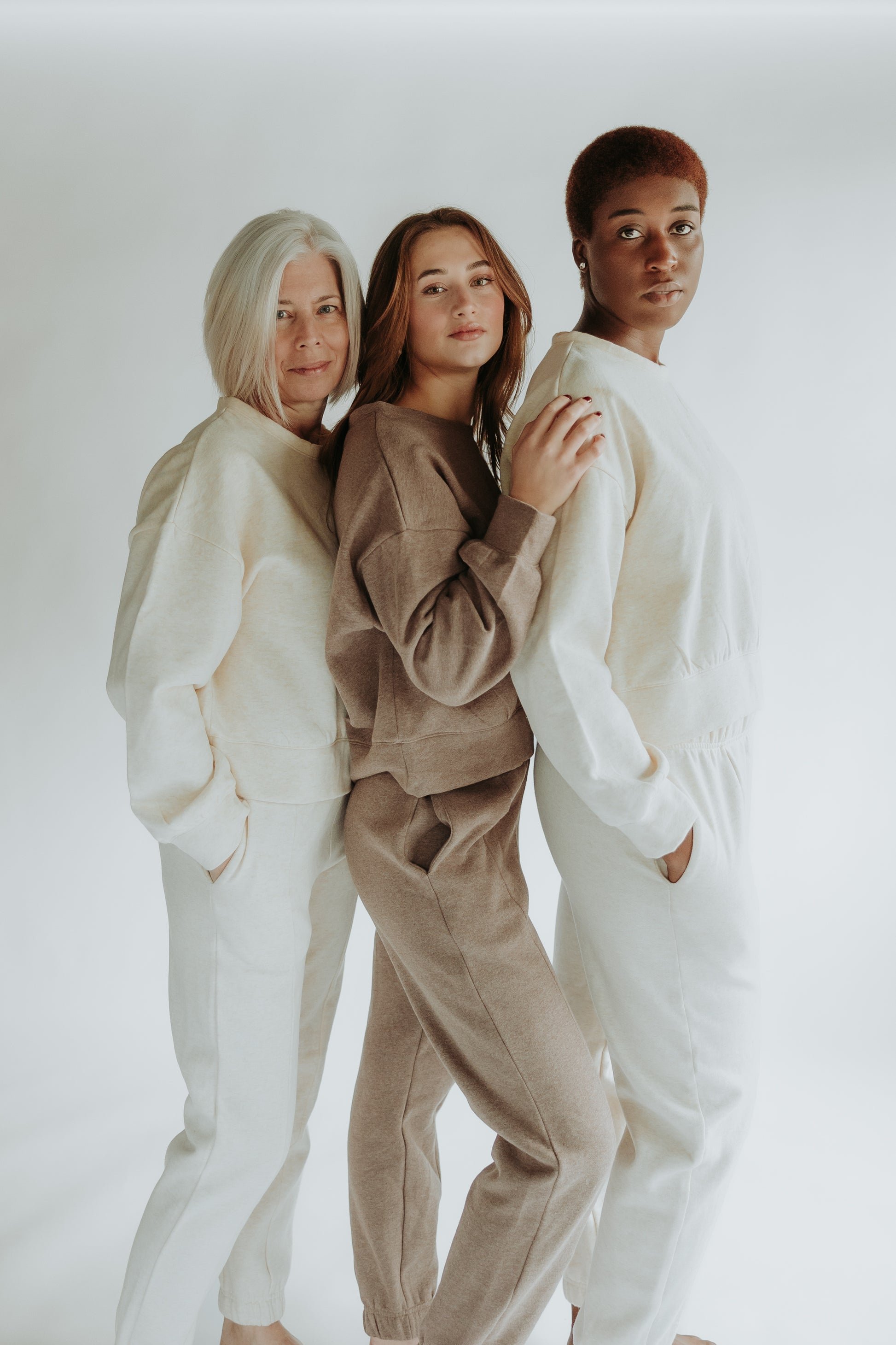 Three women are smiling at the camera, standing, and wearing the classic flee set in two different colors : beige and chocolate brown
